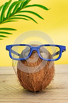 A cocnut wearing blue glasses on tropical yellow background. Summer and trave concept