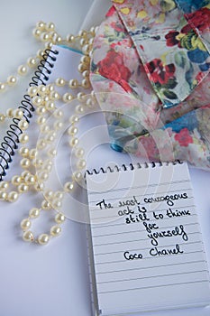 Coco Chanel quotes written on a block note, pearl accessories and an silky flower shirt photo