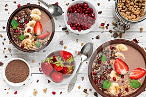 Cocoa or chocolate and banana protein smoothie bowls with granola, strawberry and pomegranate seeds served for breakfast