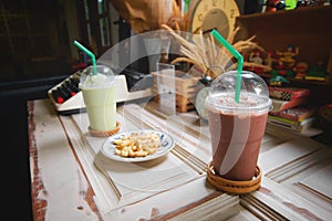 Cocoa, Chocolate and Green tea milk frappe in clear plastic glass have green straw and Alphabet cookies on wood shelf at cafe. photo