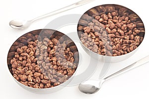 Cocoa coated puffed rice in metal bowls on white