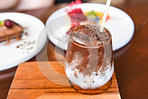 Cocoa drink and chocolate - tasty milk shake with ice cocoa in glass on wood background