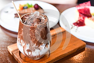 Cocoa drink and chocolate - tasty milk shake with ice cocoa in glass on wood background