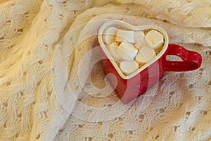 Cocoa or hot chocolate in a red circle with heart shaped marshmallows on knit background