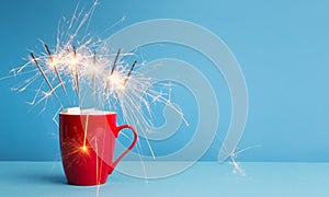 Cocoa and marshmallow in Red cup with sparklers on blue