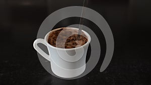 Cocoa powder is poured into a white cup with milk and stirred with a spoon