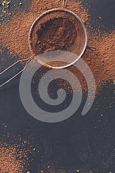 Cocoa powder in a sieve over black slate background