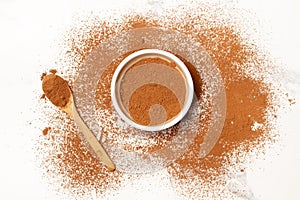 Cocoa powder in a white bowl, on a wooden spoon and on a marble kitchen counter