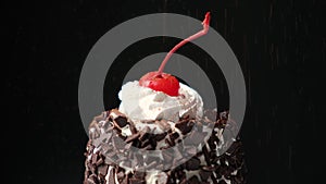 Cocoa is sprinkled on a chocolate cake with glazed cherries and cream on a black background