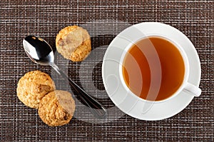 Coconut cookies  spoon  cup with tea on saucer on mat. Top view