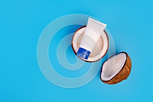 Coconut cream in plastic tube with fresh coconut split in half on isolated blue background.