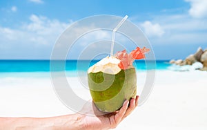 Coconut drink in palm hand on a tropical beach La Digue Seychelles Islands