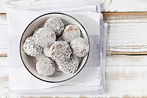 Coconut energy balls in a white cup on a light wooden background.