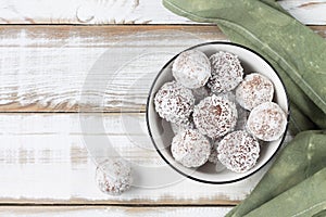 Coconut energy balls in a white cup on a light wooden background. Top view