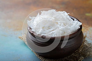 Coconut flakes in a clay bowl on a blue background