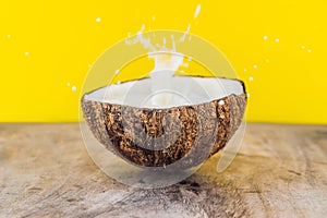 Coconut fruit and milk splash inside it on yellow background