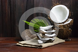 Coconut half with coconut pieces and leaf on wooden table