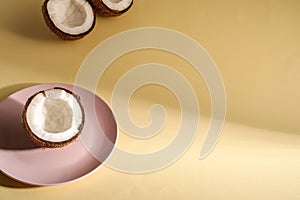 Coconut half in pink plate with nut fruits on cream yellow plain background, abstract food tropical concept