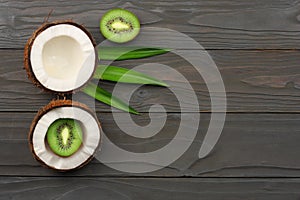 Coconut with kiwi fruit and green leaves on dark wooden background. top view with copy space