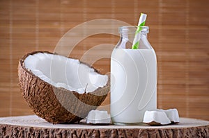 Coconut milk in glass bottle with tubule on natural brown background