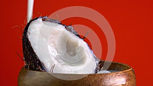 Coconut milk pouring, dripping coconut water, drops of coconuts oil over red background. Cracked fresh coconut with