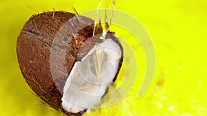 Coconut milk pouring, dripping coconut water, drops of coconuts oil over yellow background. Cracked fresh coconut with