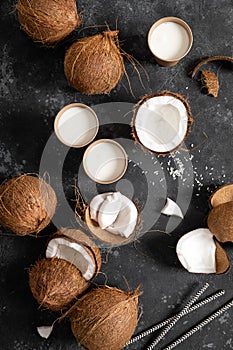 Coconut milk, whole and cracked coconuts on black background