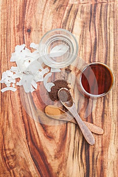 Coconut oil, coconut rashes, ground vanilla beans and maple sirup on a wooden background