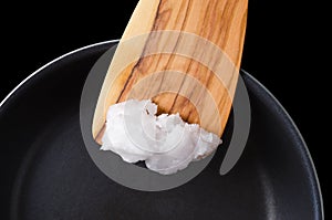 Coconut oil on wooden spatula over coated pan