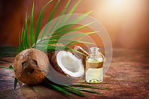 Coconut palm oil in a bottle with coconuts and green palm tree leaf on brown background. Coco nut closeup. Healthy Food, skin care