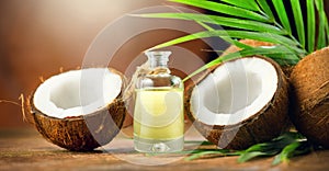 Coconut palm oil in a bottle with coconuts and green palm tree leaf on brown background. Coco nut closeup. Healthy food, skincare