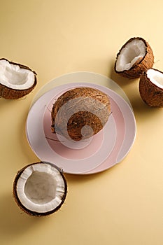 Coconut in pink plate with nut fruits on cream yellow plain background, abstract food tropical concept