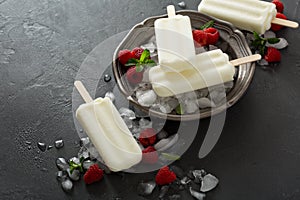 Coconut popsicles with raspberries on black background