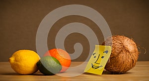 Coconut with post-it note smiling at citrus fruits