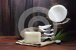 Coconut soap with coconut half and coconut pieces and leaf on wooden table.