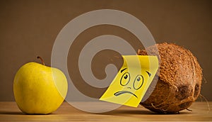 Coconut with sticky post-it note looks sadly at apple