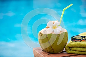 coconut with a straw on the edge of a deckchair against a blue w