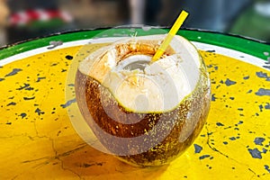 Coconut water. Fresh coconut with straw, sitting on vibrant yellow table