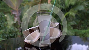 Coconuts and coconut water on the black glass table isolated over blurred palm trees background