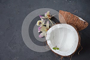 Coconuts with mint and orhid flowers, on dark background. Copy space.