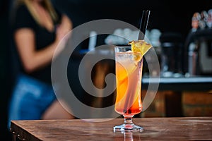 Coctail drink with pinapple in a night bar. Blurred woman in the background