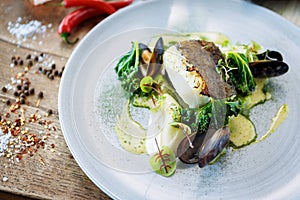 Cod fillet with cauliflower cream, asparagus, clam-wine sauce and mussles. Delicious seafood fish closeup served on a