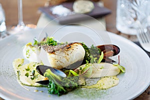 Cod fillet with cauliflower cream, asparagus, clam-wine sauce and mussles. Delicious seafood fish closeup served on a