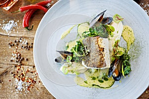 Cod fillet with cauliflower cream, asparagus, clam-wine sauce and mussles. Delicious seafood fish closeup served on a