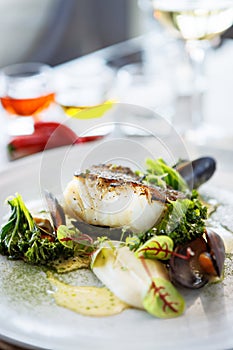 Cod fillet with cauliflower cream, asparagus, clam-wine sauce and mussles. Delicious seafood fish closeup served on a