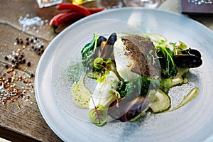 Cod fillet with cauliflower cream, asparagus, clam-wine sauce and mussles. Delicious seafood fish closeup served on a