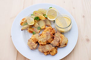 Cod fish in batter or cod fritters served with baked potatoes with parsley leaves and home made mayonnaise sauce.