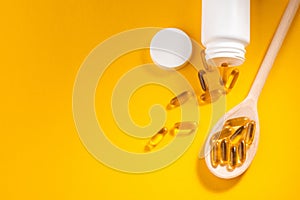 Cod liver oil capsules in a spoon and a bottle on orange background