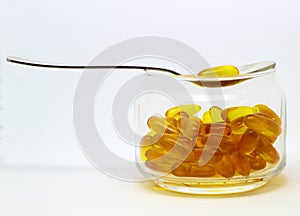 Cod liver oil omega 3 vitamin e gel capsules isolated on white background in a transparent glass bottle with a steel spoon