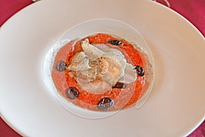 cod in salad with black olive and tomato on white plate